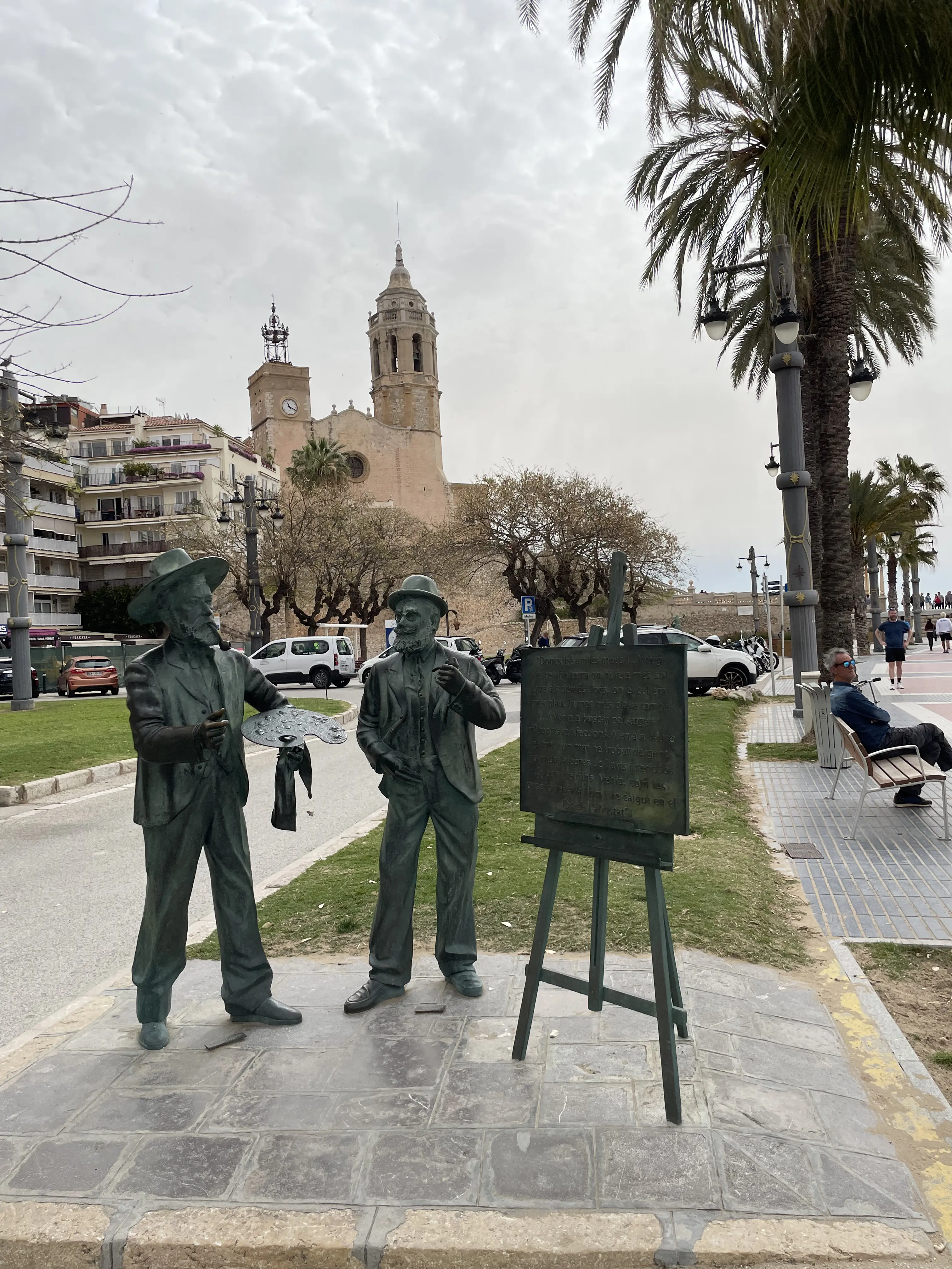 Estatuas de Santiago Rusiñol y Ramon Casas junto a un caballete con poesía en el paseo marítimo